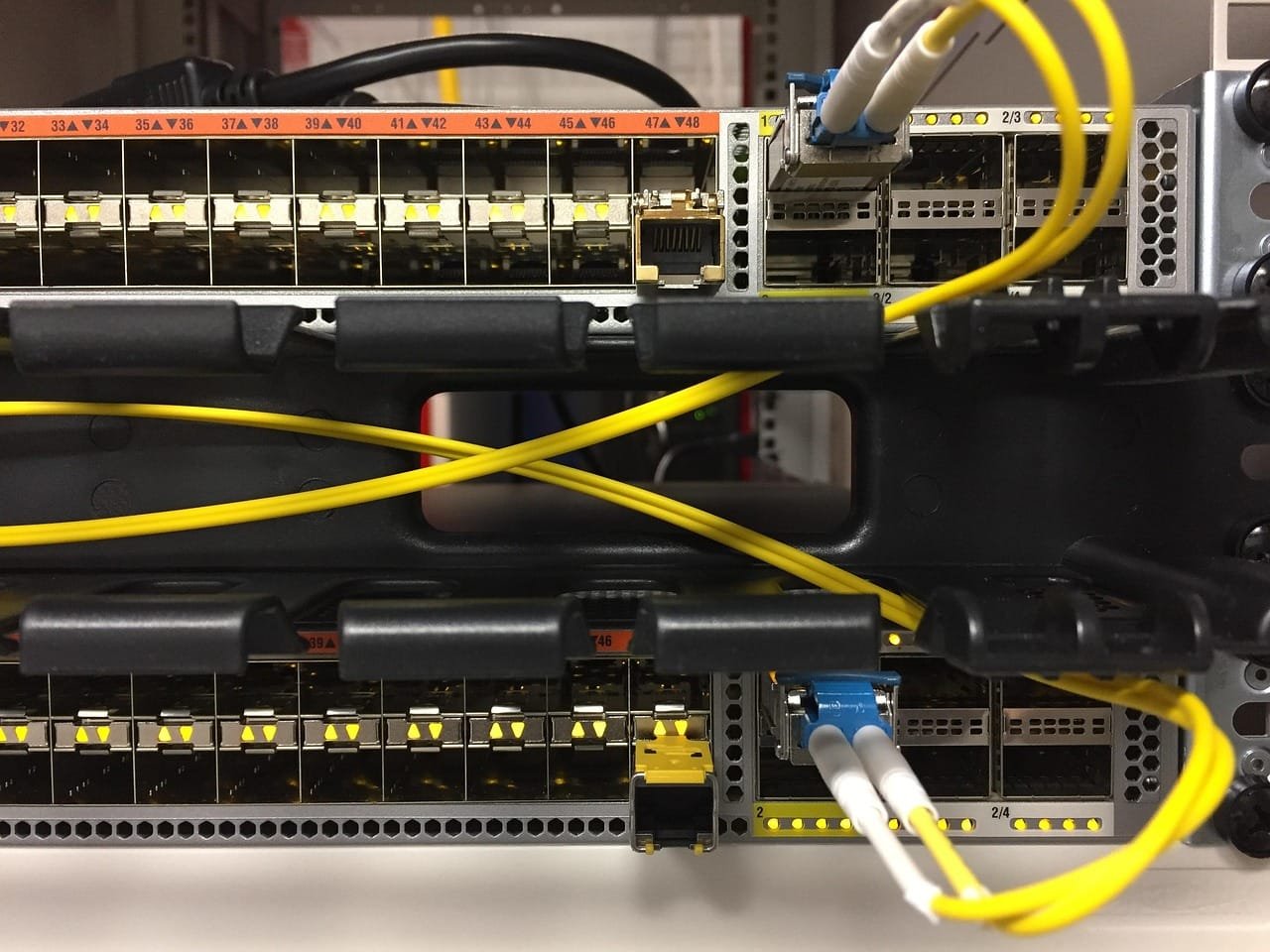 A data center server rack with multiple network cables in yellow and black colors neatly organized and connected to networking equipment, showing professional cable management and modern server infrastructure.